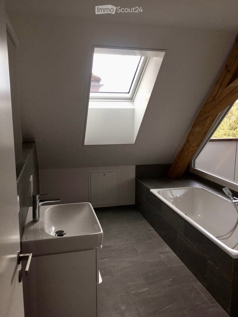 Modern bathroom with a sleek sink, faucet, and bathtub, featuring large windows and grey tiles.