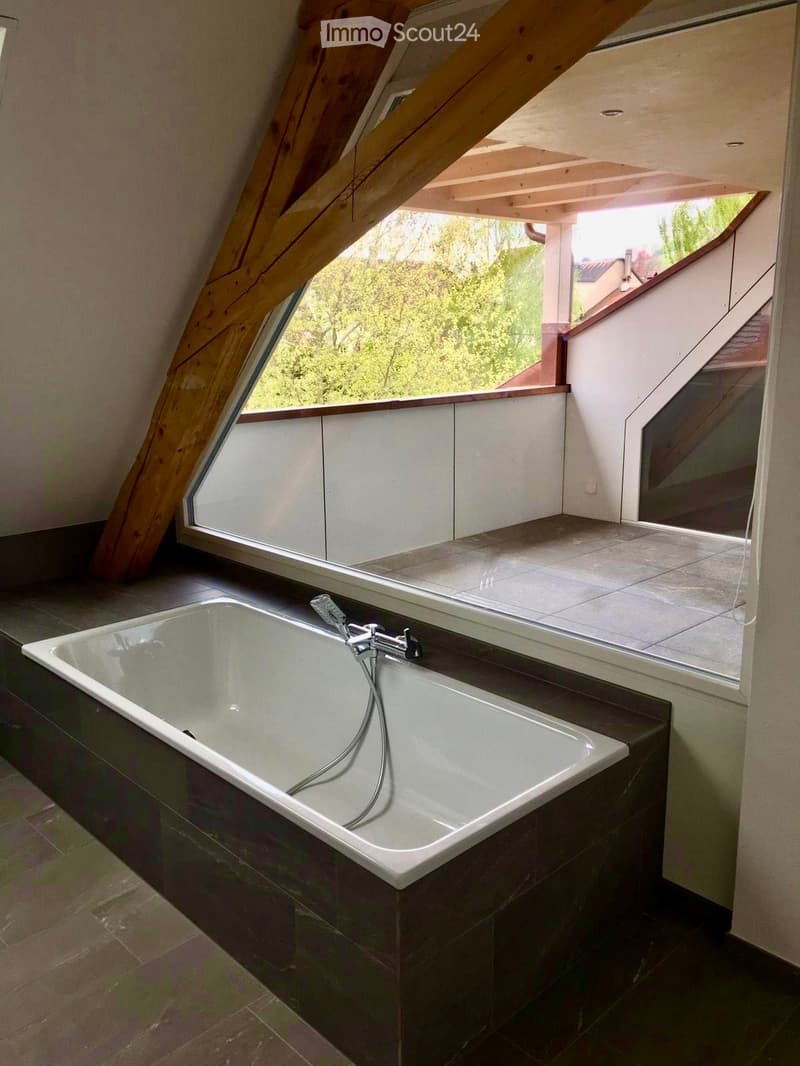 Modern bathroom with a freestanding bathtub, sleek faucet, and large window offering a view of greenery outside.