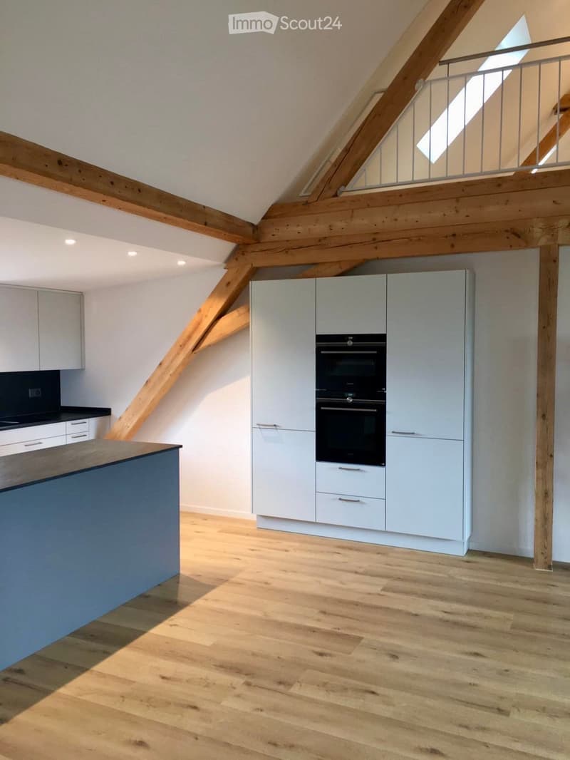 Modern kitchen with light-colored cabinets, a built-in oven, and a wooden countertop, featuring exposed wooden beams and a wooden floor.