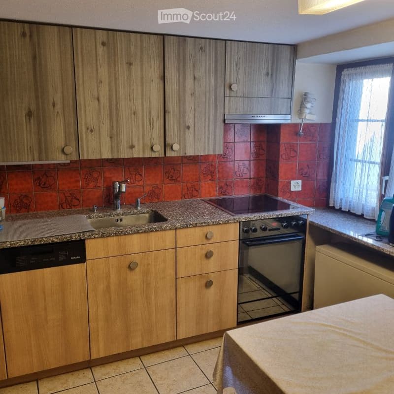 A modern kitchen with wooden cabinets, granite countertops, a sink with a faucet, an oven, and a dishwasher. The backsplash features a red tile design with decorative patterns.