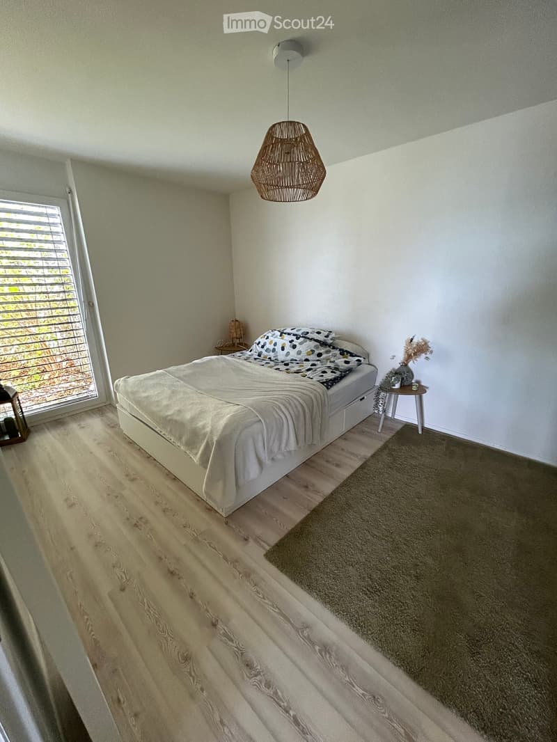 Modern bedroom with a large bed, nightstand, small table with vase, and a hanging wicker lamp.