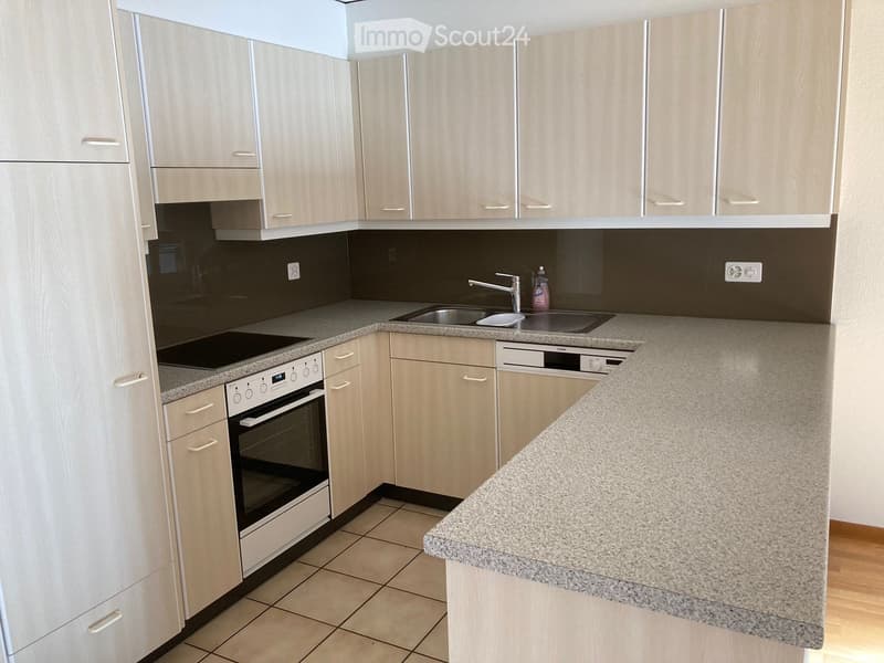Modern kitchen with light wood cabinets, granite countertops, and stainless steel appliances including an oven, sink, and dishwasher.