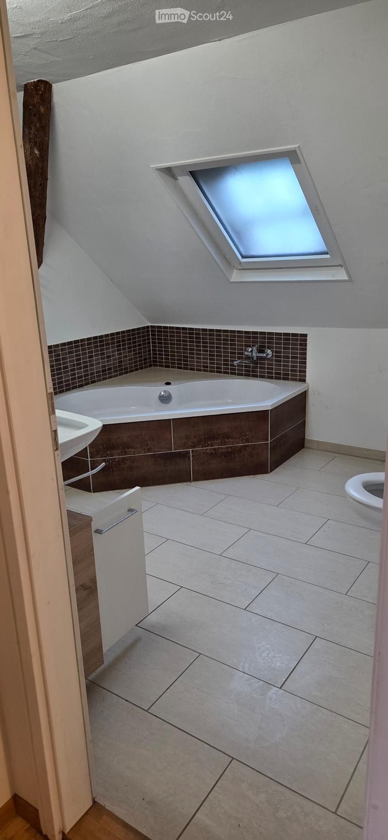 Modern bathroom with a bathtub, toilet, sink, and a skylight window above the tub.