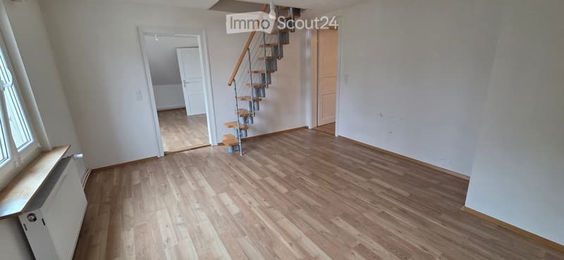 Empty room with wooden flooring, white walls, and a staircase leading to another level. The room has a window on one side and doors leading to other rooms.