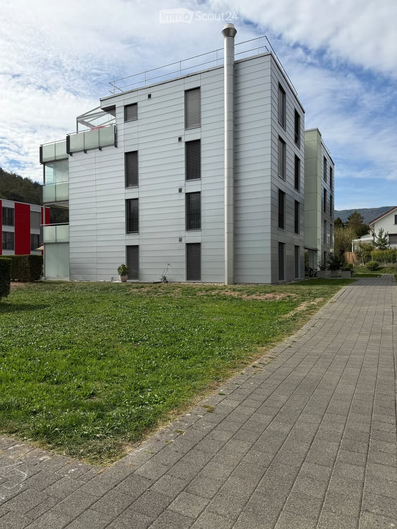 Modern two-story building with a sleek, contemporary design, featuring large windows, a balcony, and a landscaped lawn area.