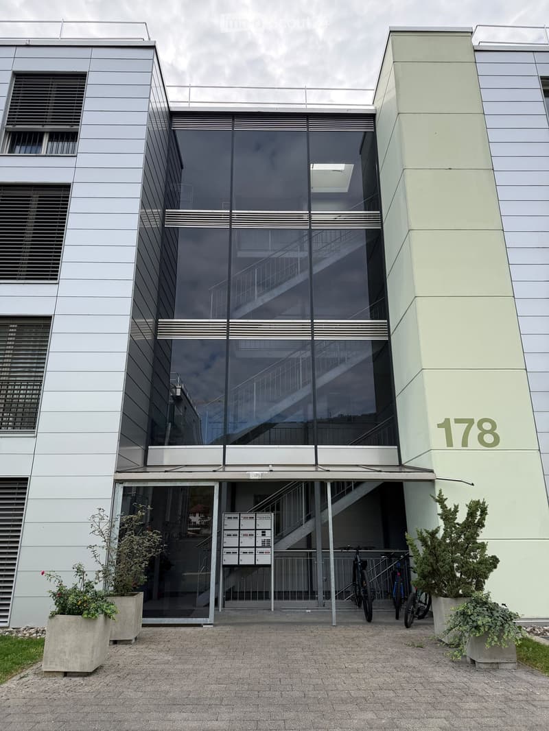 Modern building entrance with glass doors, staircase, mailboxes, and bicycles parked nearby.