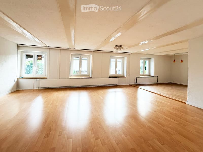 Empty room with wooden flooring, white walls, large windows, and radiators. No furniture or equipment present.
