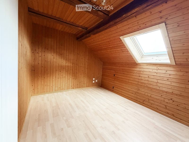 Empty room with wooden walls and ceiling, light wooden floor, skylight window, and exposed wooden beams.