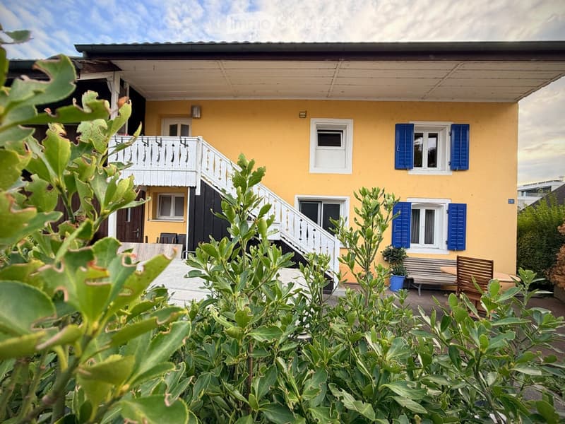 Two-story yellow house with white trim, blue shutters, and a white balcony staircase leading to the upper level.