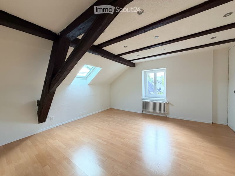Empty attic room with wooden beams, wooden flooring, skylight window, and radiator.
