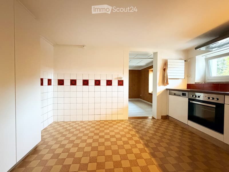 Empty kitchen with white tiled walls, checkered flooring, and built-in appliances including an oven and dishwasher. A doorway leads to another room.