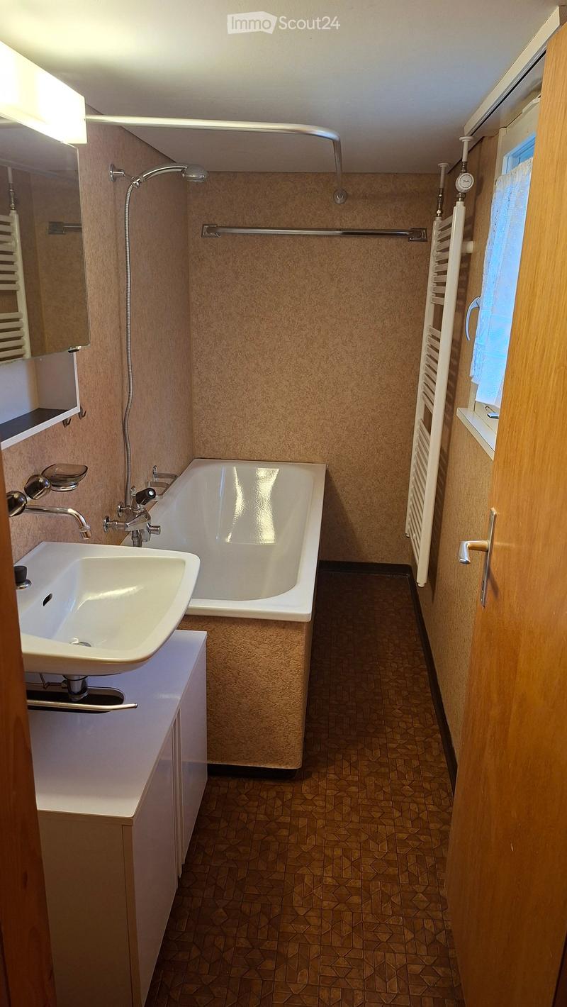 Modern bathroom with a white sink, bathtub, showerhead, mirror, radiator, and tiled floor.