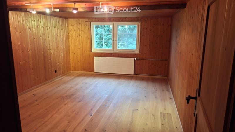 Empty room with wooden walls and floor, featuring a window and a radiator.