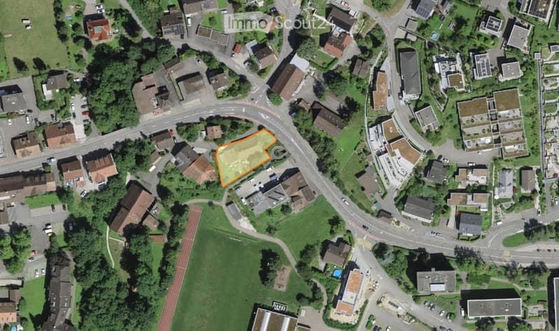Aerial view of a residential area with multiple houses, roads, and green spaces. The highlighted area in orange suggests a specific plot or property of interest.