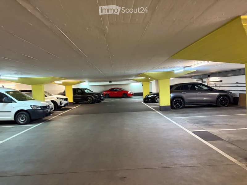 Underground parking area with several parked cars, yellow pillars, and concrete floors.