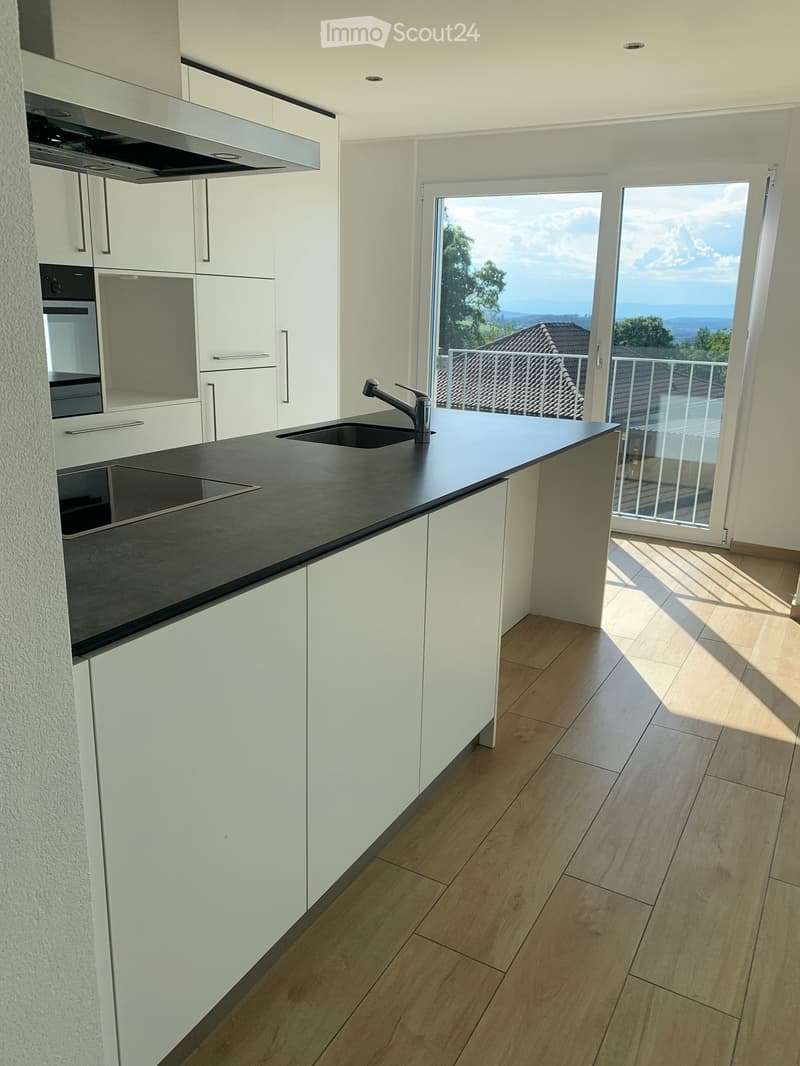 Modern kitchen with white cabinets, black countertop, sink, faucet, and built-in oven. Large window offers a scenic view.