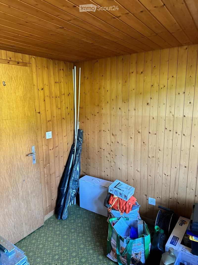 A small wooden-paneled room with a refrigerator, bags, and various items scattered around.