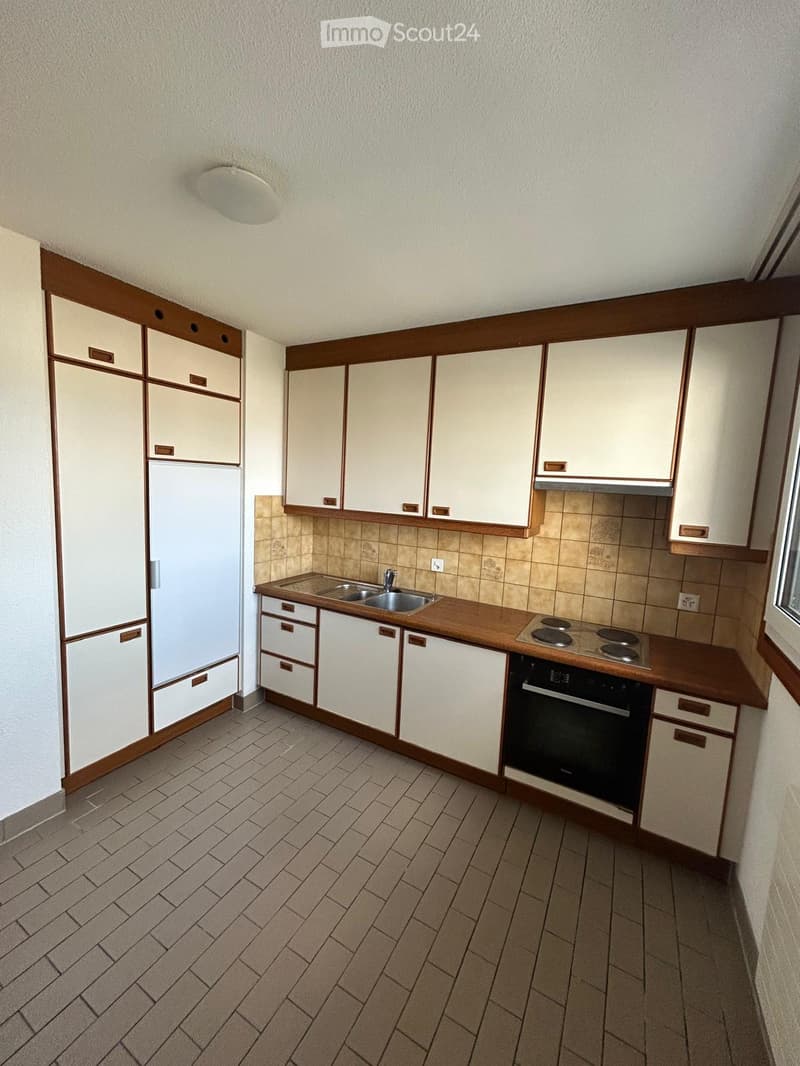A compact kitchen with white cabinets, a wooden countertop, a sink, a stove, and an oven. The floor is tiled, and the walls are painted white with a wooden trim.