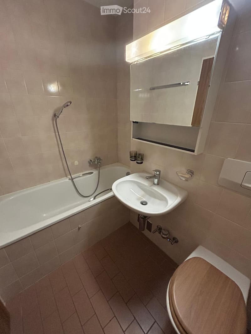 Bathroom with beige tiles, bathtub, sink, toilet, and a mirror cabinet above the sink.