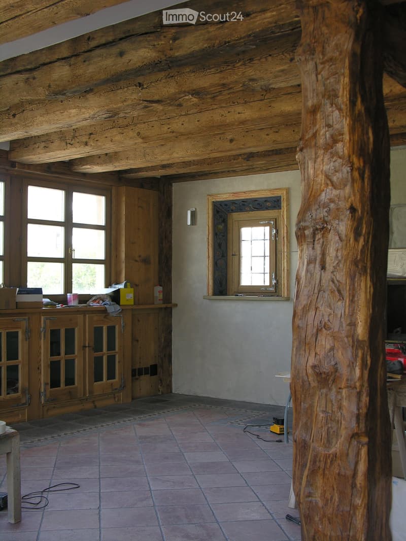 Large wooden support beam, wooden floor, white walls, large window, wooden cabinets