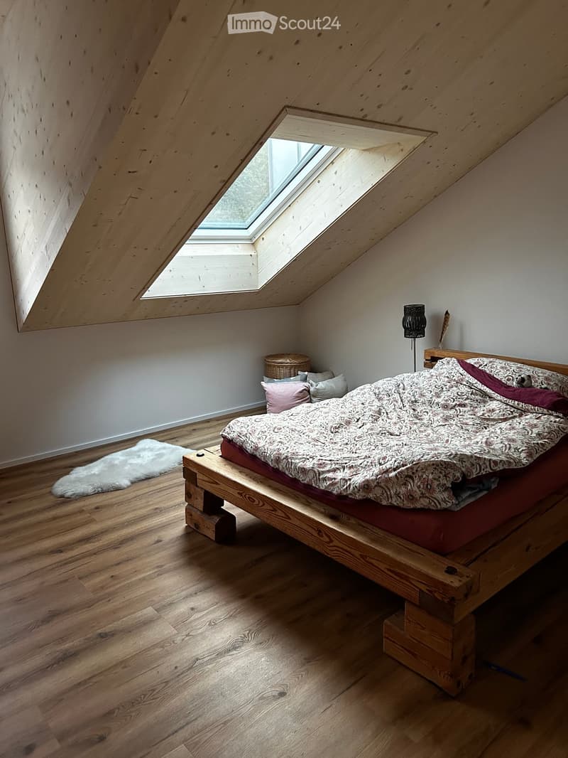 Cozy attic bedroom with wooden bed, patterned bedding, nightstand, floor lamp, and skylight window.