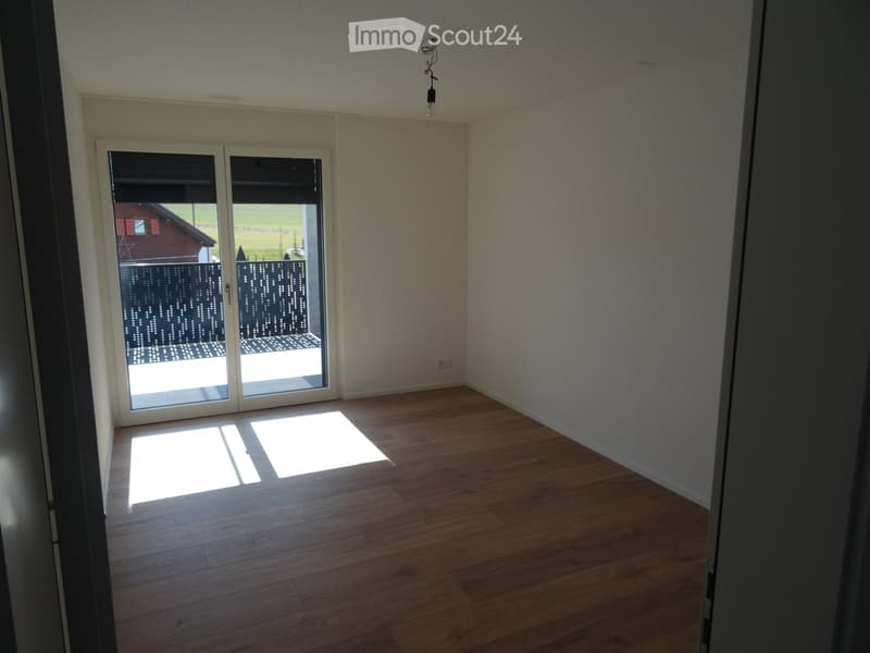 Empty room with wooden flooring, large sliding glass doors leading to an outdoor area, and natural light streaming in.