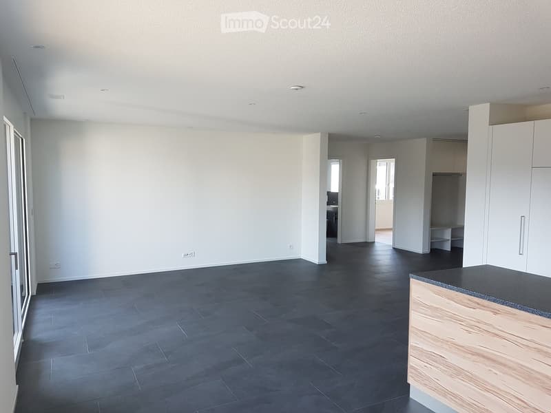 Empty room with dark grey tiled floor, white walls, and a small wooden counter in the corner. No furniture or equipment present.