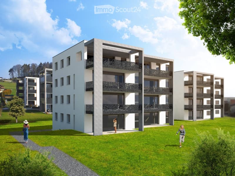 Modern multi-story residential building with balconies, surrounded by green lawn and trees.