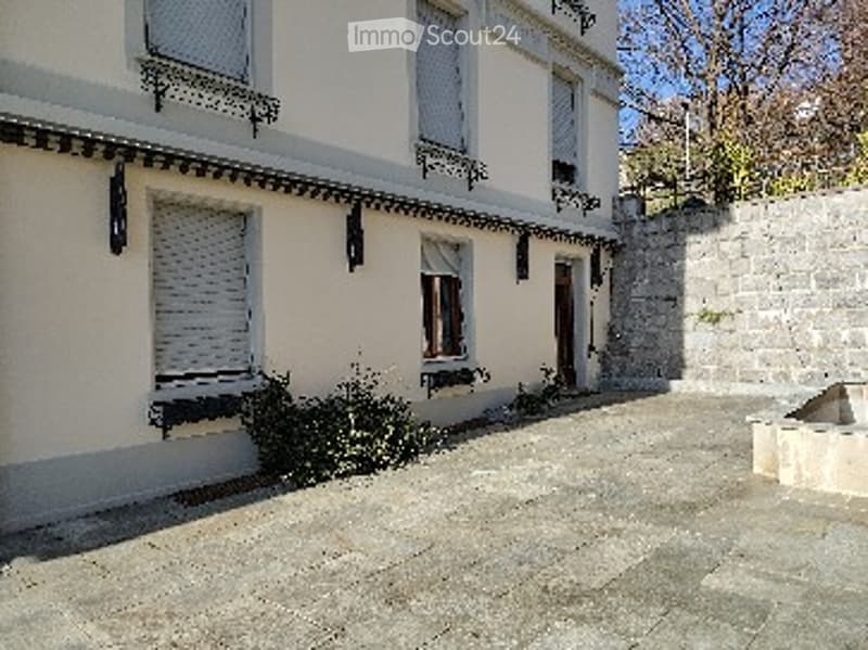 A two-story white building with multiple windows, shutters, and a stone pathway leading to the entrance.
