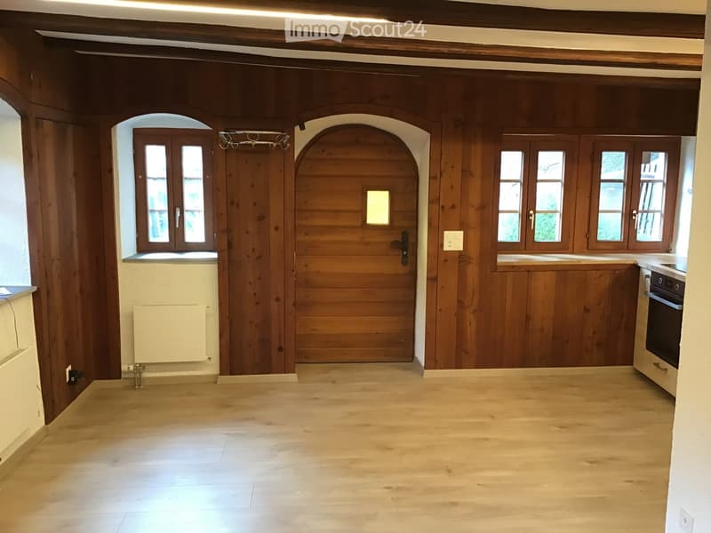 Empty room with wooden walls, wooden floor, large windows, and a radiator. No furniture or equipment present.