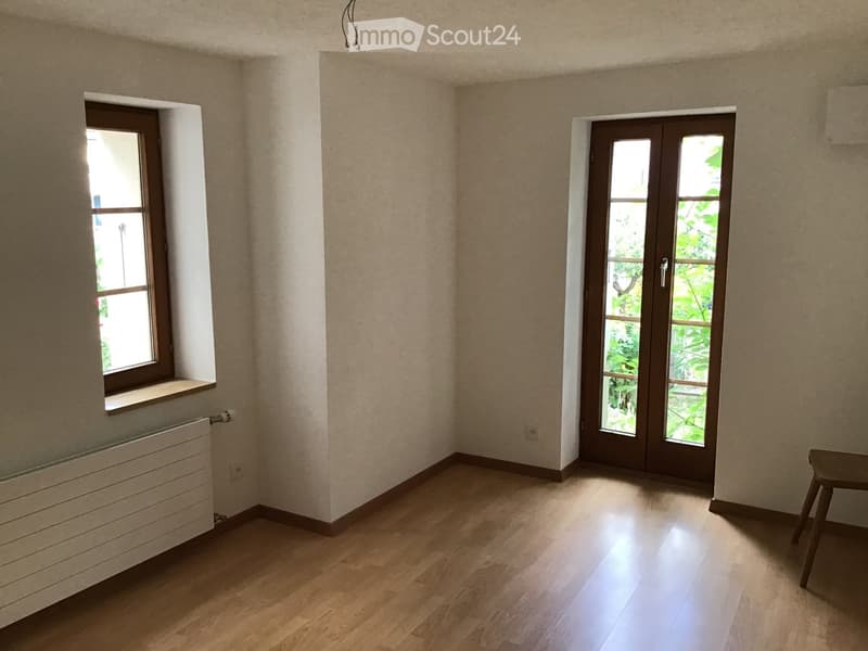 Empty room with wooden flooring, beige walls, a window with a radiator below, and a glass door leading outside.