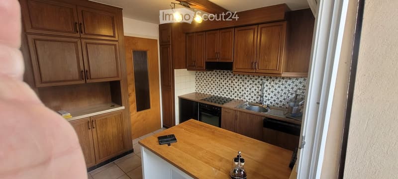 Wooden kitchen with cabinets, a sink, an oven, and a dishwasher. The countertop has a bottle and a small item on it.