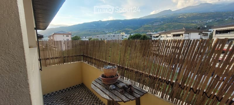 Balcony with wooden fence, small wooden table, potted plant, and scenic mountain view.