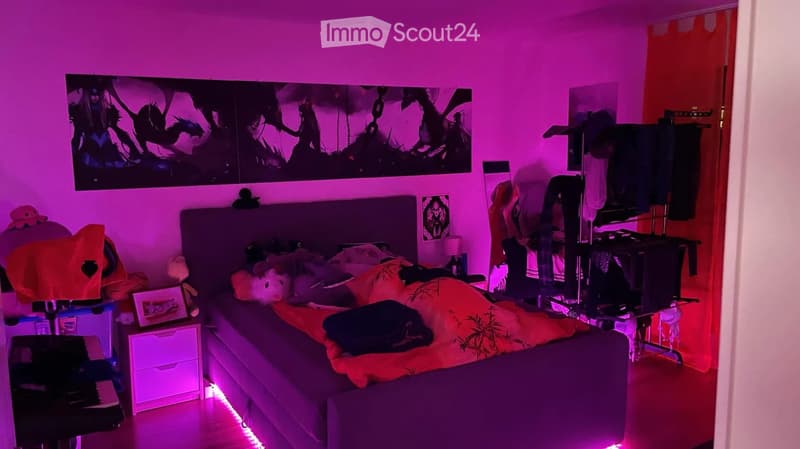 A bedroom with a large bed, nightstand, picture frame, stool, chair, table, and lamp. The room is illuminated with purple lighting.