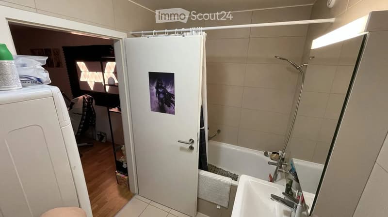 Bathroom with a bathtub, showerhead, faucet, mirror, and washing machine visible in the adjacent room.