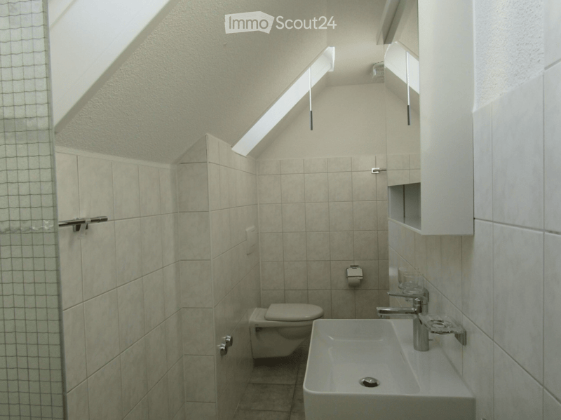 Compact bathroom with a toilet, sink, and mirror. Light-colored tiles and a small window provide natural light.