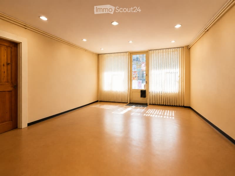 Empty hallway with wooden door, frosted glass door, and vertical blinds. Light-colored walls and floor, recessed ceiling lights.
