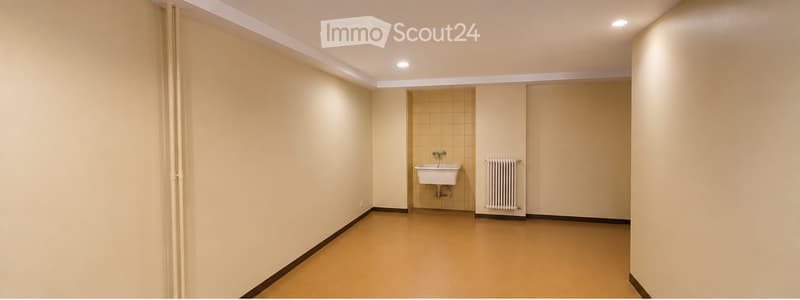 Empty room with beige walls, tiled section, sink, radiator, and light fixtures.