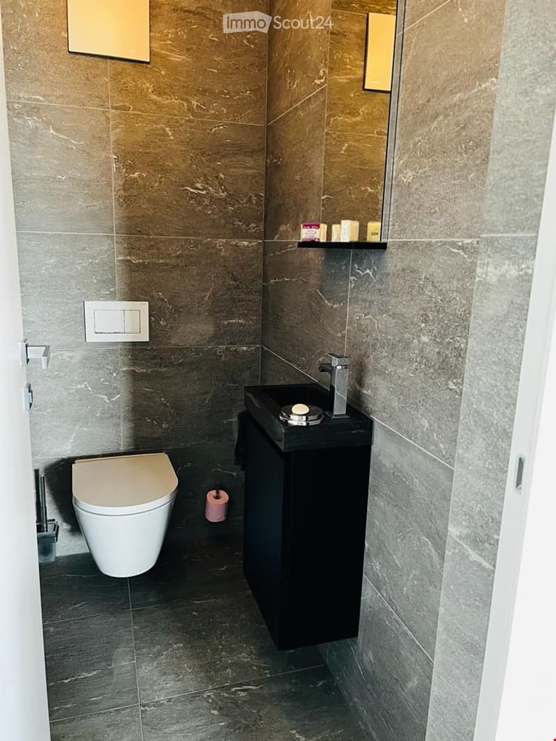 Modern bathroom with dark grey marble tiles, a white toilet, a black sink cabinet, a chrome faucet, and a mirror above the sink.