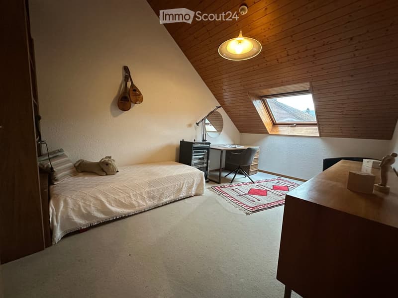 Cozy attic bedroom with slanted wooden ceiling, bed, desk, chair, mirror, and decorative guitar on wall.