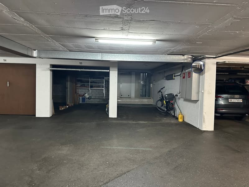 Underground parking area with concrete floors and walls, featuring numbered parking spaces, a bicycle, and a car parked in one of the spaces.