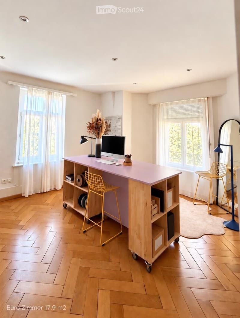 Bright, modern office space with wooden flooring, large windows, a pink desk, two yellow chairs, a floor lamp, and a mirror.