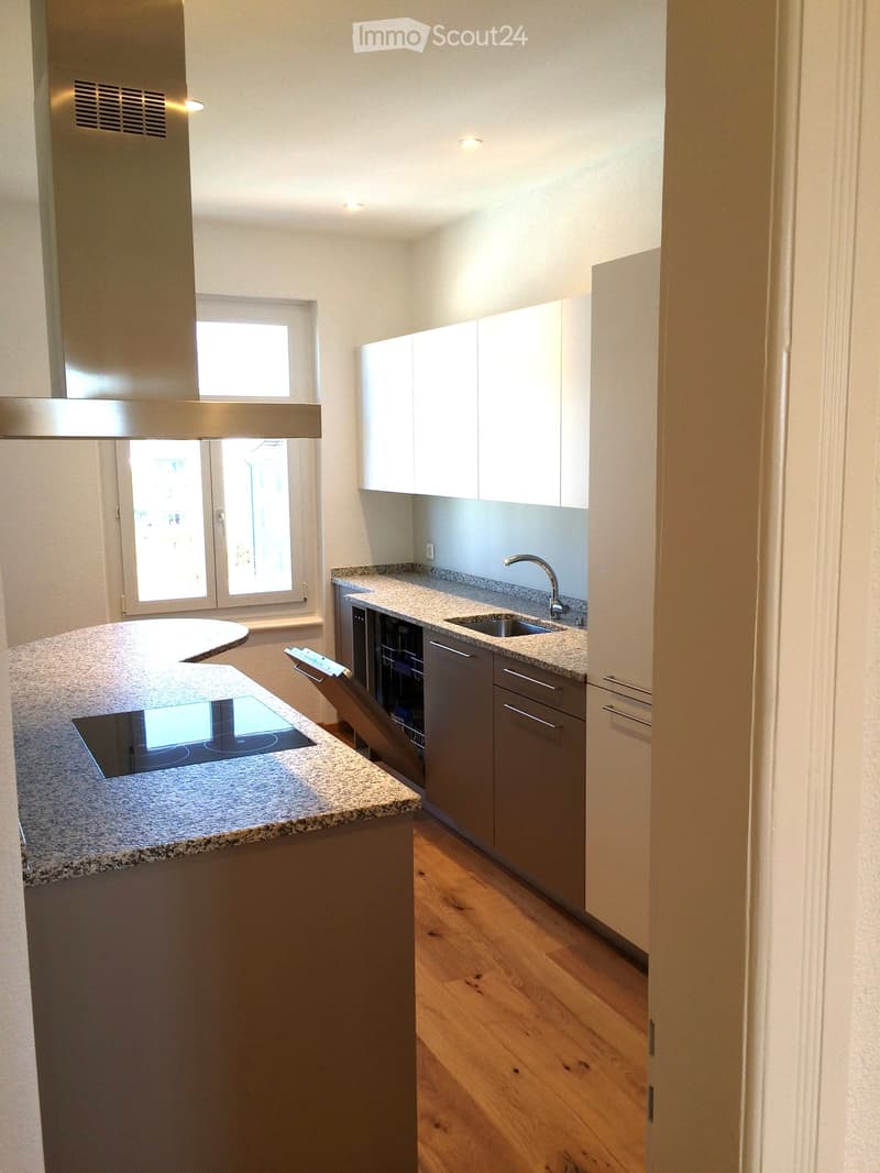 Modern kitchen with a central island, induction cooktop, sink, dishwasher, and white cabinets.