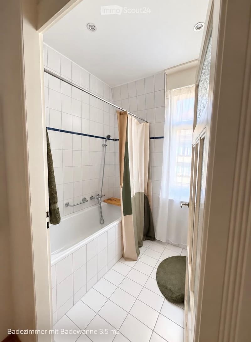 Bathroom with a bathtub, shower curtain, towel, and a small green rug on the floor.