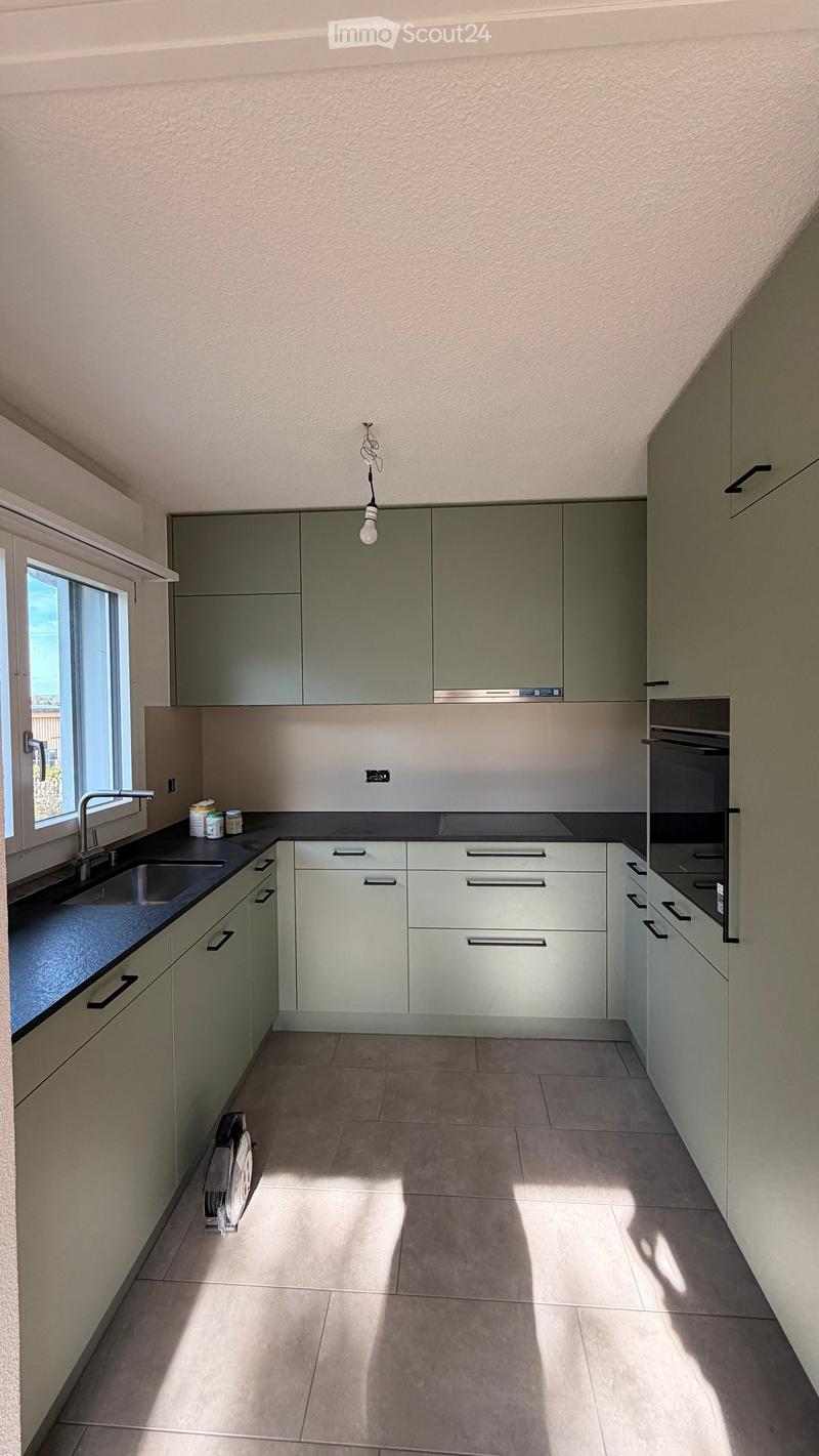 Modern kitchen with grey cabinets, white countertops, and a large window. Includes a sink, faucet, and an oven.