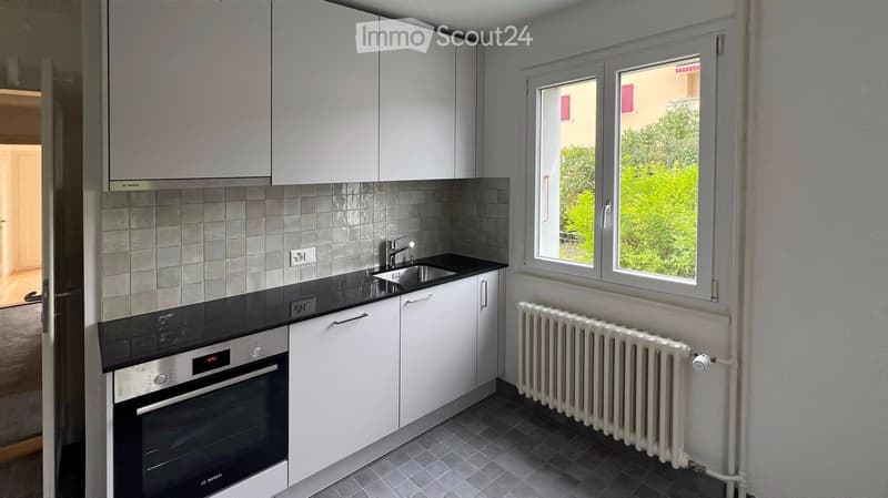Modern kitchen with white cabinets, black countertops, stainless steel oven, sink, and radiator.