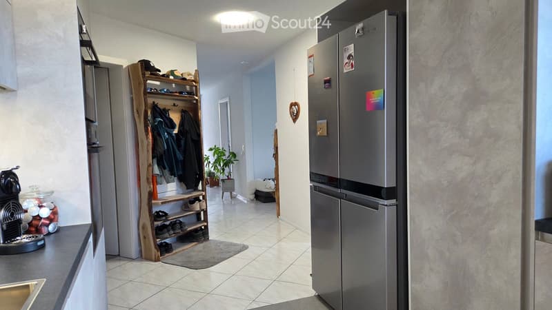 A modern hallway with a wooden shoe rack, a refrigerator, a coffee machine on the counter, and a small plant in the corner.