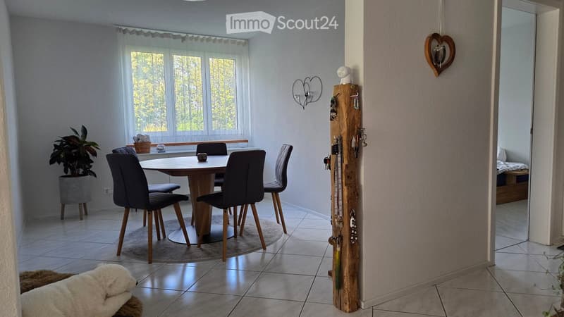 Dining area with a round wooden table, four black chairs, a potted plant, and a key holder with keys and a heart-shaped wall decoration.
