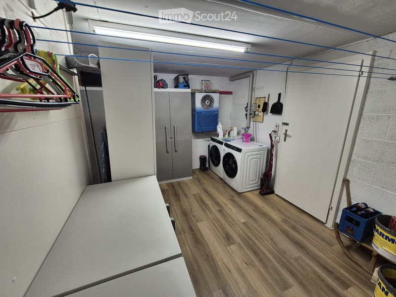 Utility room with wooden flooring, white cabinets, washing machine, dryer, fan, and various storage items.