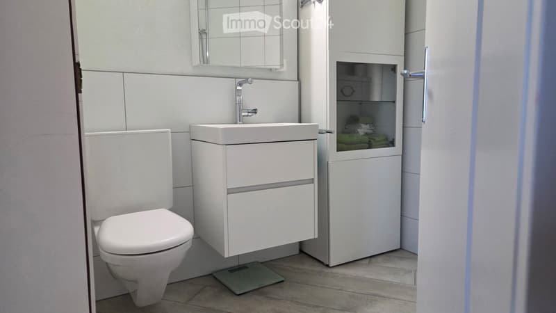 Modern bathroom with white tiles, a toilet, a sink with a modern faucet, a mirrored cabinet, and a built-in storage cabinet with towels inside.